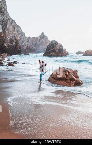 Giovane donna che salta dalla roccia a Praia da Ursa, Lisboa, Portogallo Foto Stock