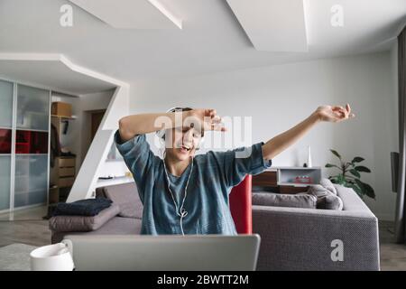 Donna felice che indossa le cuffie e usa il computer portatile a casa Foto Stock