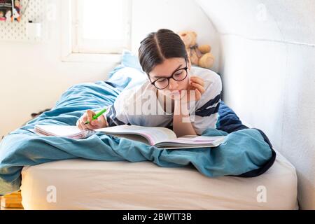 Ragazza che si steso sul letto facendo i compiti Foto Stock
