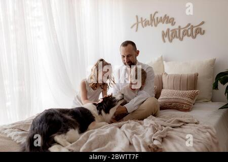 Ritratto di felice padre seduto a letto con i suoi due figli che accarezzano il cane Foto Stock