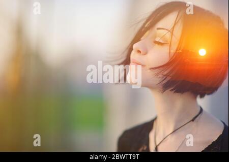 Doppio ritratto di esposizione moltiplicata di una donna sognante e simpatica meditando all'aperto con gli occhi chiusi, combinato con fotografia di natura, alba o tramonto, Foto Stock