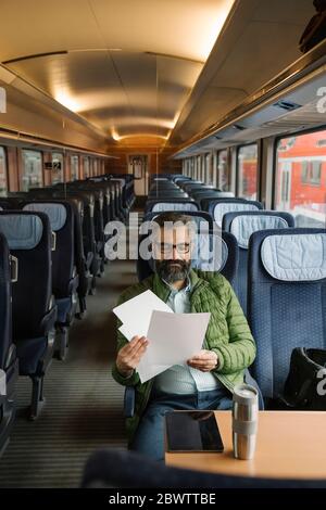 Uomo seduto in treno che legge documenti Foto Stock