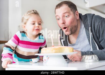 Padre e figlia che spegne le candeline sulla torta del compleanno Foto Stock