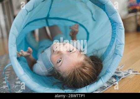 Ragazza sorridente che gioca con il tunnel di tessuto blu a casa Foto Stock