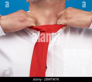 l'uomo in una camicia bianca da ufficio strappa un filo rosso satinato dal collo su sfondo blu, concetto di depressione, disoccupazione e licenziamento Foto Stock