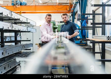 Due uomini che esaminano un pezzo di metallo in una fabbrica Foto Stock