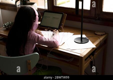 Ragazza con cuffie che disegnano fumetti manga mentre si usa un tablet computer alla scrivania in casa Foto Stock