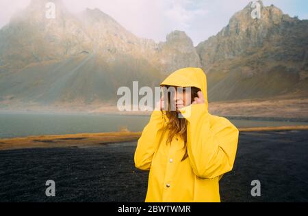 Ritratto di donna che indossa cappotto giallo in piedi sulla spiaggia di Hvalnes Nature Reserve Beach, Islanda Foto Stock