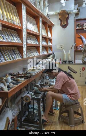 Feng Huang, Cina - Agosto 2019 : Artigianato femminile che lavora in un negozio di souvenir facendo vari articoli dall'avorio e da altre ossa e parti animali Foto Stock