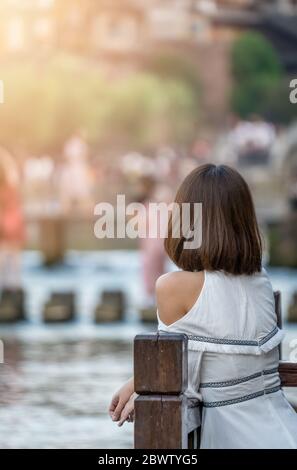 Feng Huang, Cina - Agosto 2019 : bella giovane donna cinese vestita di vestito bianco appoggiata sulla barriera di legno e che posa per una foto sulla Th Foto Stock