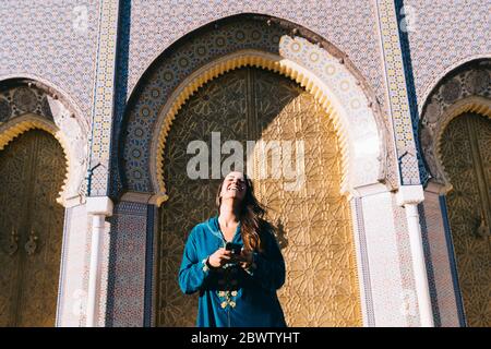 Giovane donna in piedi davanti a un tradizionale architure con abito marocchino, Marocco Foto Stock