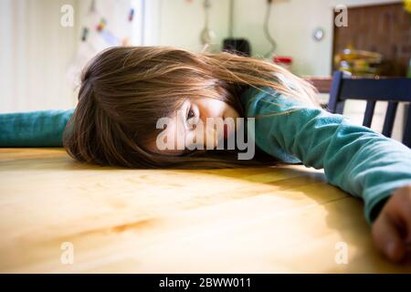 Ragazza annoiata che si stendeva sul tavolo da cucina Foto Stock