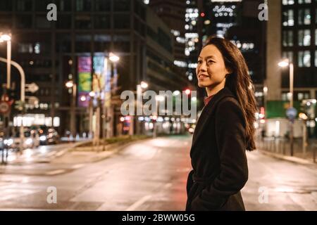 Giovane donna che attraversa la strada in città di notte, Francoforte, Germania Foto Stock