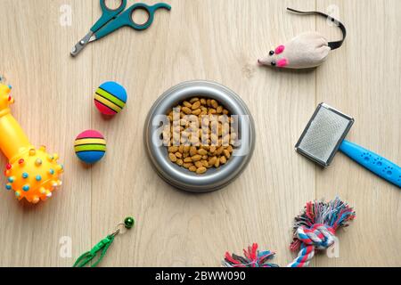 Ciotola con cibo secco kibble e accessori per gatti su tavolo di legno. Vista dall'alto del concetto di cura e formazione degli animali domestici. Negozio veterinario banner mockup. Foto Stock