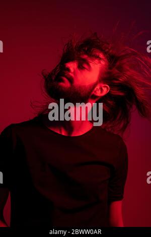 Ritratto di giovane illuminato rosso su sfondo rosso che gli lancia i capelli Foto Stock