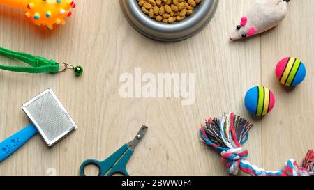 Strumenti per la cura degli animali domestici sulla vista dall'alto del tavolo in legno. Composizione piatta con accessori per cani e gatti e ciotola con cibo secco kibble. Negozio veterinario banner mocku Foto Stock