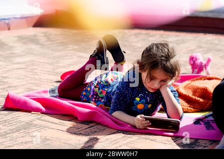 Ritratto di bambina che giace su coperta sul tetto guardando smartphone Foto Stock