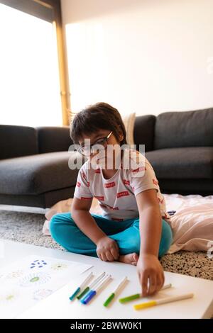 Ritratto di ragazzo seduto sul pavimento a casa disegnando fiori Foto Stock