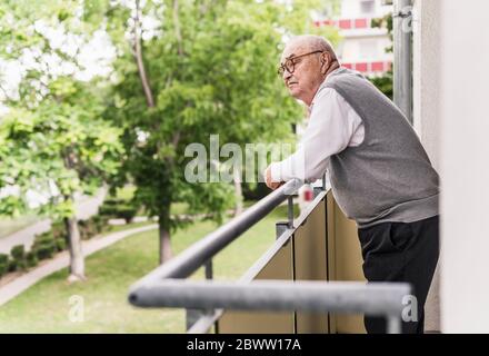 Uomo anziano in piedi sul balcone che guarda lontano Foto Stock