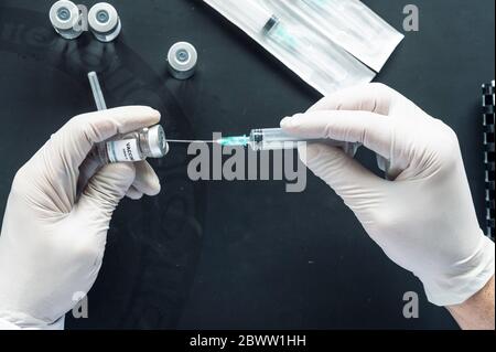 Immagine ritagliata della siringa per iniezione manuale del medico nel flaconcino di vaccinazione sul computer portatile della scrivania del laboratorio Foto Stock