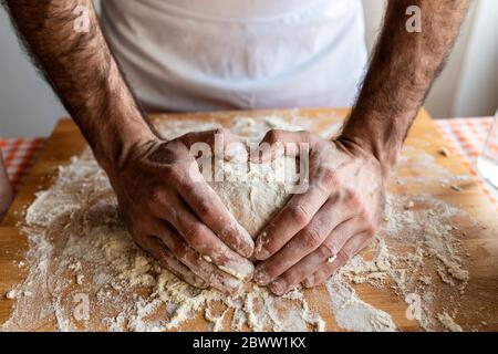 Le mani dell'uomo che modellano il cuore sulla palla da impasto Foto Stock