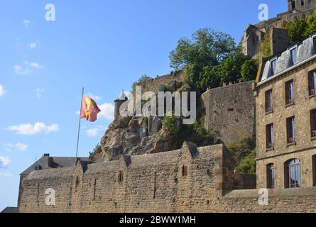 Mont St Michel, Francia, mura fortezza e architettura storica, con la bandiera e stemma della Normandia Foto Stock