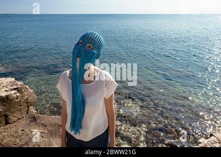 Donna che indossa un ricamo blu con frange in piedi davanti al mare guardando in su Foto Stock