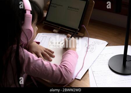 Ragazza che indossa le cuffie che impara la lingua cinese mentre usa il tablet digitale alla scrivania Foto Stock
