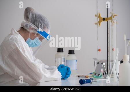 Scienziato stanco in abbigliamento protettivo seduto alla scrivania Foto Stock