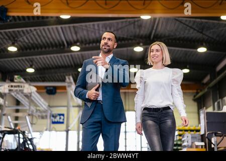 Uomo d'affari e giovane donna che cammina e parla in una fabbrica Foto Stock