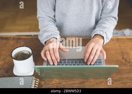 Donna che lavora su un computer portatile, con una tazza di tè sul lato Foto Stock