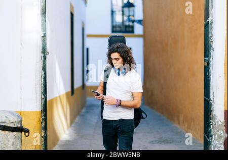 Giovane uomo che usa il telefono cellulare mentre cammina su una strada stretta a Santa Cruz, Siviglia, Spagna Foto Stock