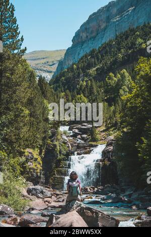 Spagna, Provincia di Huesca, escursionista femminile ammirando la piccola cascata sul fiume di montagna limpido Foto Stock