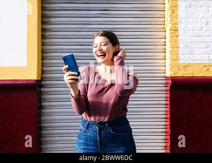 Donna felice che usa uno smartphone in un edificio della città Foto Stock