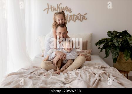 Ritratto di famiglia di felice padre seduto a letto con i suoi due figli Foto Stock
