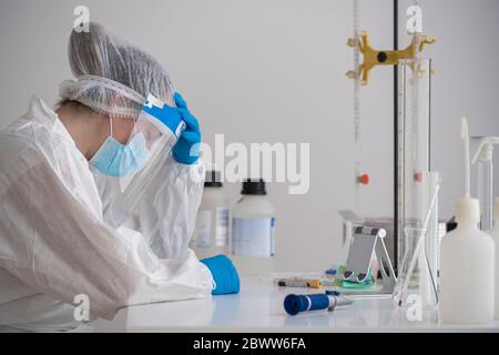 Scienziato stanco in abbigliamento protettivo seduto alla scrivania Foto Stock