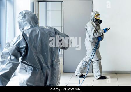 Personale addetto alla pulizia che desinfetta l'ospedale da virus scandalosi, indossando indumenti protettivi Foto Stock