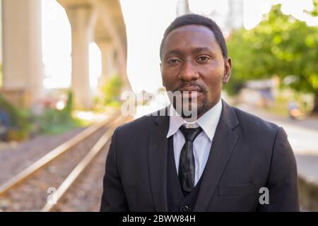 Faccia di bell'uomo d'affari africano sopportato alla stazione ferroviaria all'aperto Foto Stock