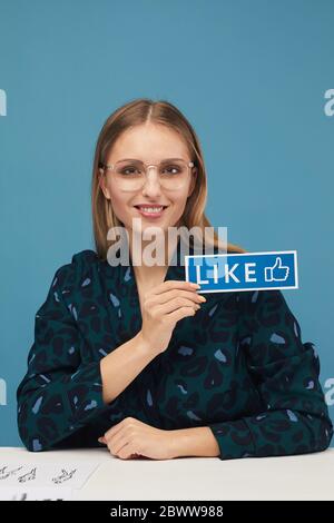 Ritratto di giovane bella donna che tiene il cartello e sorridendo alla macchina fotografica contro lo sfondo blu Foto Stock