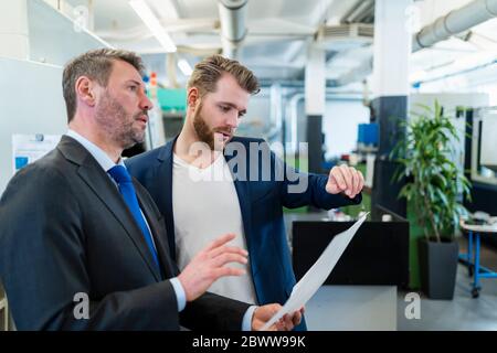 Due uomini d'affari che hanno un incontro di lavoro in una fabbrica che discute un piano Foto Stock