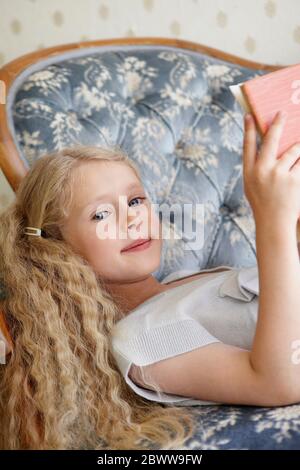 Ritratto di una ragazza che si stendeva su un divano leggendo un libro Foto Stock