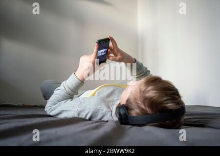 Ragazzo con le cuffie che si stendono a letto usando il telefono cellulare Foto Stock