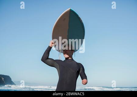 Surfista portatore di handicap che porta la sua tavola da surf in testa Foto Stock