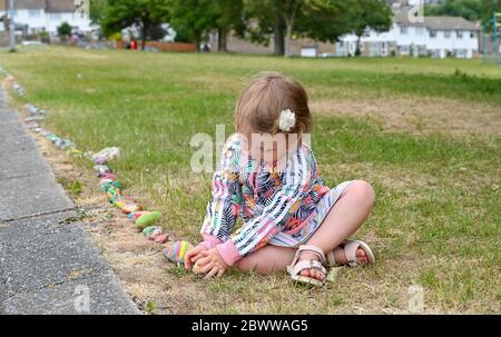 Brighton UK 3 giugno 2020 - Isabella Lloyd, di tre anni, aggiunge il suo ciottolo dipinto al serpente di roccia, creato con centinaia di ciottoli dipinti dai bambini nel parco di Lockwood Woodingdean vicino a Brighton . I serpenti di roccia sono comparsi intorno al paese durante la crisi pandemica del coronavirus COVID-19 alcuni ringraziano l'NHS e i lavoratori chiave. Credit: Simon Dack / Alamy Live News Foto Stock