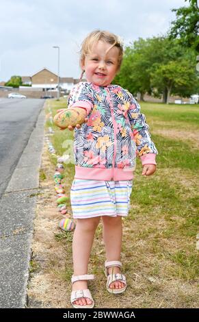 Brighton Regno Unito 3 giugno 2020 - la bambina di tre anni aggiunge il suo ciottolo dipinto al serpente di roccia che è stato creato con centinaia di ciottoli dipinti da bambini a Lockwood Park Woodingdean vicino Brighton . I serpenti di roccia sono apparsi in tutto il paese durante la crisi pandemica del coronavirus COVID-19 , alcuni ringraziano il servizio sanitario nazionale e i lavoratori chiave . Crediti: Simon Dack / Alamy Live News Foto Stock