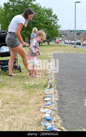 Brighton UK 3 giugno 2020 - Isabella Lloyd, di tre anni, aggiunge il suo ciottolo dipinto al serpente di roccia, creato con centinaia di ciottoli dipinti dai bambini nel parco di Lockwood Woodingdean vicino a Brighton . I serpenti di roccia sono comparsi intorno al paese durante la crisi pandemica del coronavirus COVID-19 alcuni ringraziano l'NHS e i lavoratori chiave. Credit: Simon Dack / Alamy Live News Foto Stock