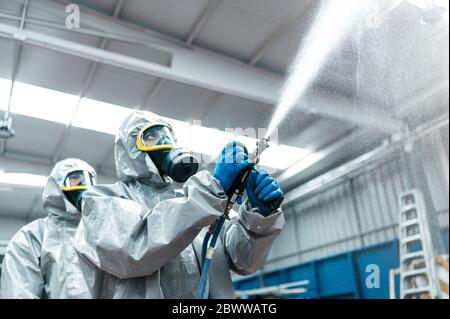 Vista ad angolo ridotto degli operatori sanitari che spruzzano sostanze chimiche dal tubo flessibile in magazzino Foto Stock