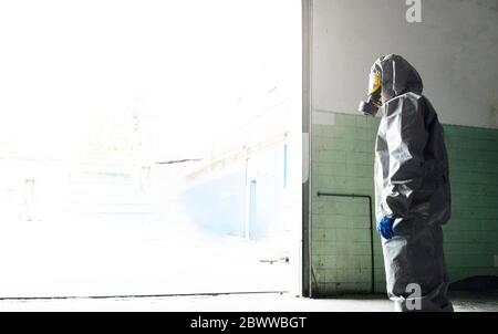 Vista laterale dell'operatore sanitario in piedi in indumenti da lavoro protettivi all'ingresso del magazzino Foto Stock