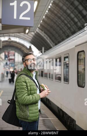 Uomo con panino alla stazione ferroviaria Foto Stock