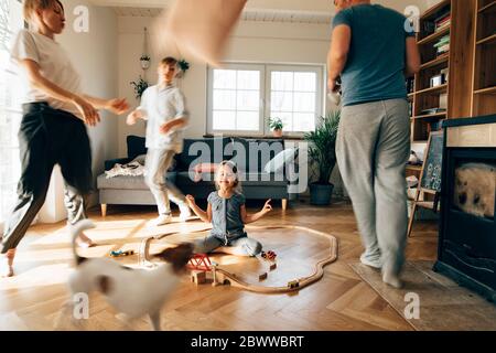 Bambina meditating nel mezzo dei giocattoli, mentre la famiglia sta correndo intorno a lei Foto Stock